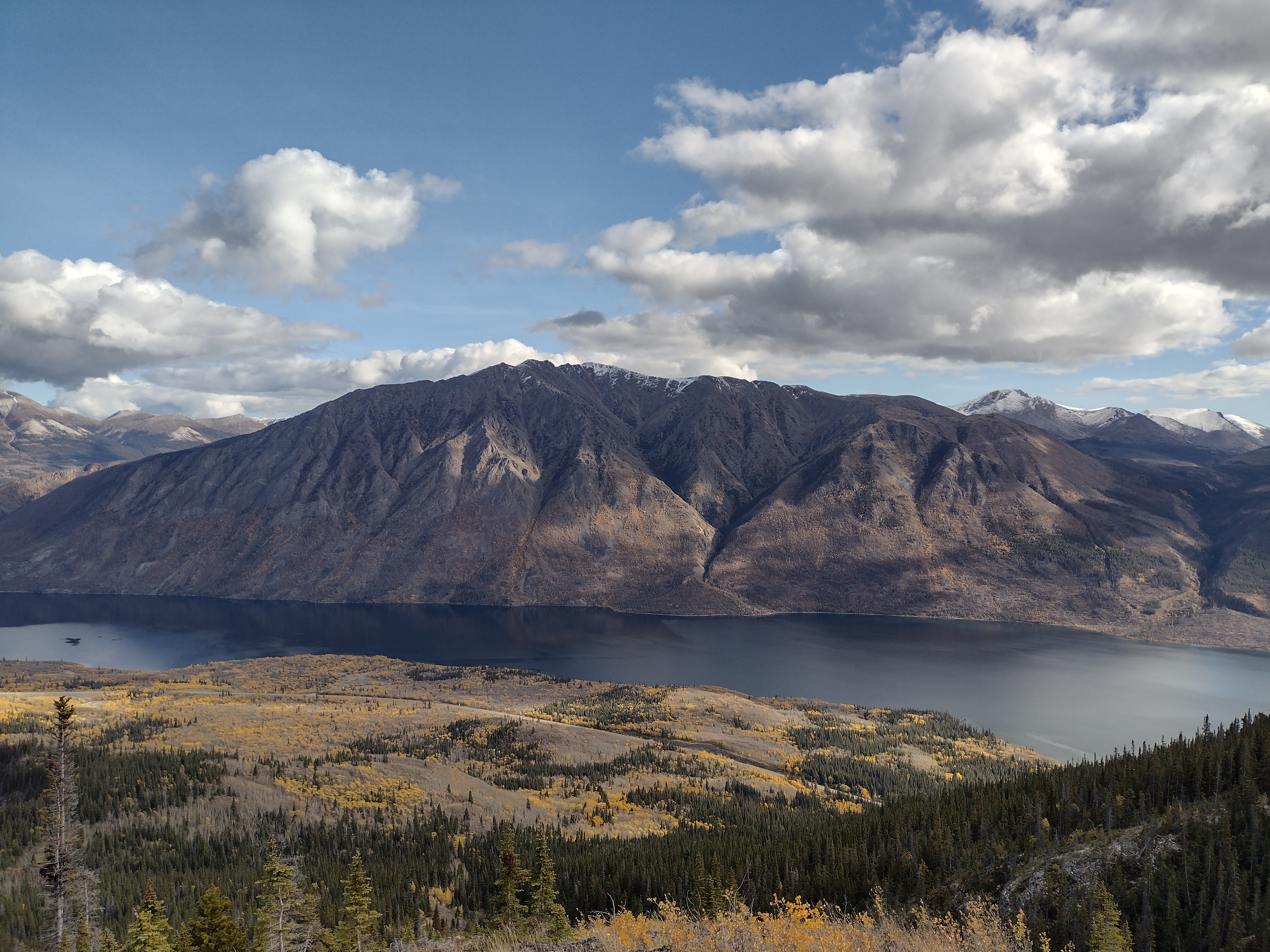 Dramatic Yukon mountain rising above a lake with golden fall foliage on the slopes below